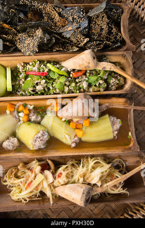 Array di tipico autentica Lao cibo: alghe cracker (Khaipaen), Larp, riempiti i cetrioli e papaia insalata servita nei tradizionali piatti di bambù. Foto Stock