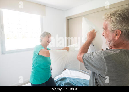 Felice di età compresa tra i caucasici senior adulto giovane godetevi la mattina presto fare una guerra di cuscini insieme a giocare e ridere un sacco. amore e sposato da sempre li Foto Stock