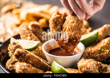 Close-up mano che tiene il pollo fritto ala con salsa di peperoncino. Foto Stock