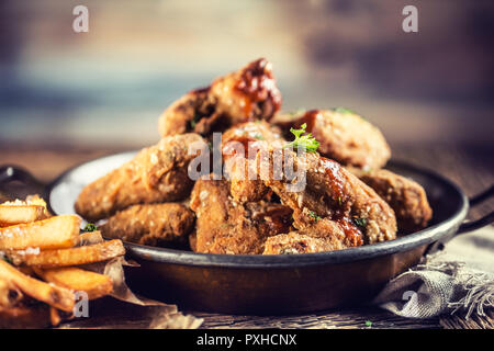 Alette di pollo fritte con patate fritte sul tavolo in pub o ristorante. Foto Stock