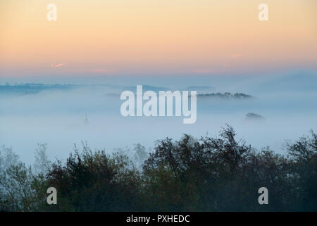 La nebbia e la nebbia a sunrise rolling sopra il villaggio Costwold di Bourton sull'acqua in autunno. Bourton sull'acqua, Cotswolds, Gloucestershire, Inghilterra Foto Stock