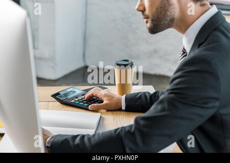 Immagine ritagliata di imprenditore utilizzando la calcolatrice in ufficio, Apri cartella sul piano portapaziente Foto Stock
