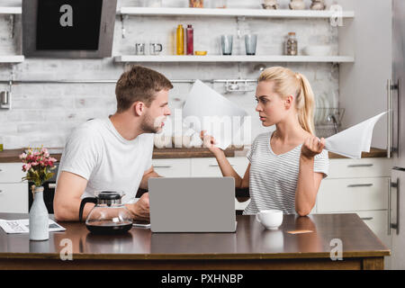 Emotional coppia giovane sostenendo e guardando ogni altra durante l'utilizzo di laptop e tenendo le carte a casa Foto Stock