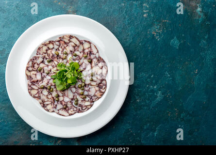 CARPACCIO di polpo. Piatti di pesce crudo fettine di polpo con olio d'oliva, limone e capperi sulla piastra bianca. Vista dall'alto. Sfondo blu Foto Stock