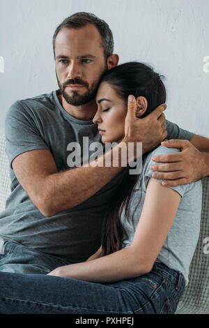 Uomo Barbuto sostenere e abbracciando sottolineato triste donna seduta sul lettino Foto Stock