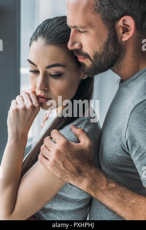 Vista laterale di uomo barbuto abbracciando e supporto di sconvolgere giovane donna Foto Stock