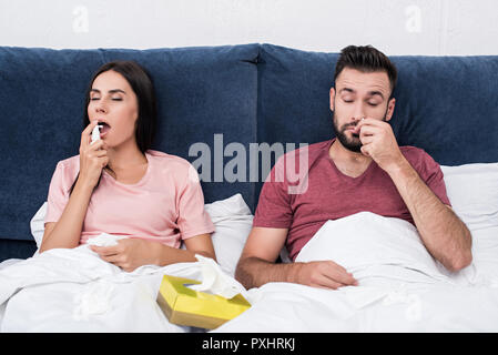 Malati matura con tosse e naso spray mentre è seduto nel letto Foto Stock