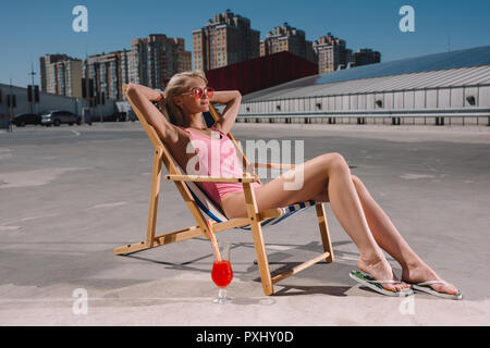 Bella giovane donna rilassante in prendisole su parcheggio Foto Stock