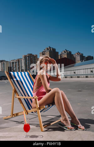 Elegante giovane donna rilassante in prendisole su parcheggio Foto Stock