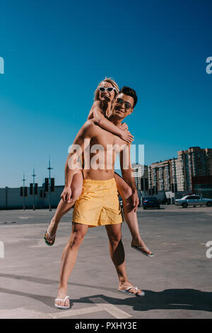 Giovane donna attraente piggybacking sul ragazzo su parcheggio Foto Stock