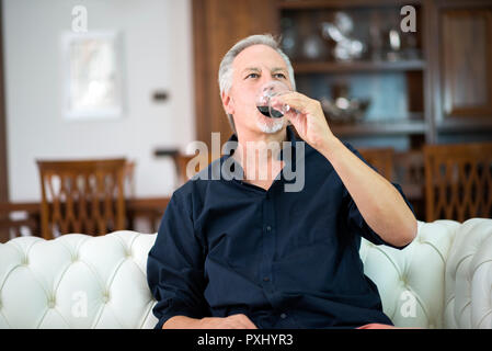 Ritratto di un uomo maturo gustando un bicchiere di vino rosso a casa Foto Stock