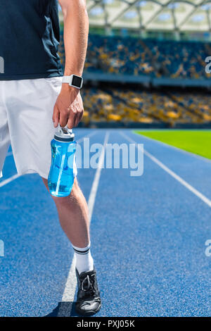 Tagliate del tiro sportivo con una bottiglia d'acqua sulla via di corsa a stadio sportivo Foto Stock