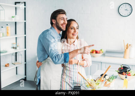 Ragazzo puntando su qualcosa alla mia ragazza durante la cottura in cucina Foto Stock