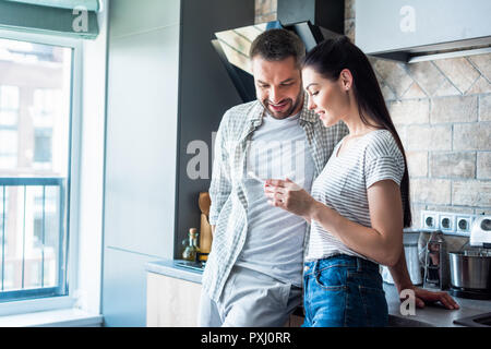 Coppia sorridente utilizza lo smartphone insieme in cucina, smart home concetto Foto Stock