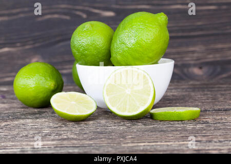 Caoticamente sparsi sul tavolo verde ripe sour limes, uno sfondo nero con una ciotola in cui giacciono i frutti, un lime viene tritato Foto Stock