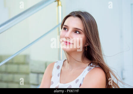 Teen ragazza con i capelli lunghi seduto sui gradini cercando fino a lato. Foto Stock