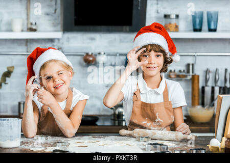 Adorabili bambini in cappelli di Babbo Natale la preparazione di biscotti di Natale e sorridente in telecamera Foto Stock