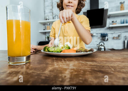 Vista ravvicinata di succo di frutta fresco in vetro e sorridente ragazzo di mangiare le verdure Foto Stock