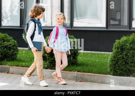 Carino piccolo scolari con zaini per mano e camminando sulla strada Foto Stock