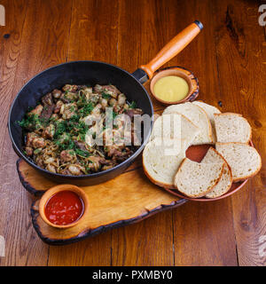 Fette di carne in una padella con il fegato, cuore e cipolle. Il bianco e il rosso e salsa di pane lungo con la padella con carne Foto Stock