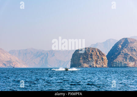 Barca galleggiante sul mare circondata da rocce nel deserto vicino a Khasab Musandam, Oman Foto Stock