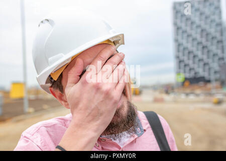 Bello un architetto o un supervisore in piedi all'aperto su un sito di costruzione tenendo un blueprint nelle sue mani Foto Stock