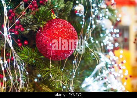 Chiudere rosso paillettes ninnolo appesi decorato con luci albero di Natale. Le decorazioni di Natale su un ramo di abete rosso. Morbida messa a fuoco selettiva, copia spac Foto Stock