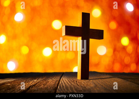 Cristiana croce di legno su blur flare luci e lo sfondo di legno Foto Stock