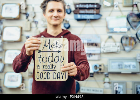 Ritratto di giovane sorridente uomo caucasico azienda messaggio motivazionale digitando sulla tavola di legno. Ogni giorno le citazioni ispiratrici concetto. In stile vintage Foto Stock