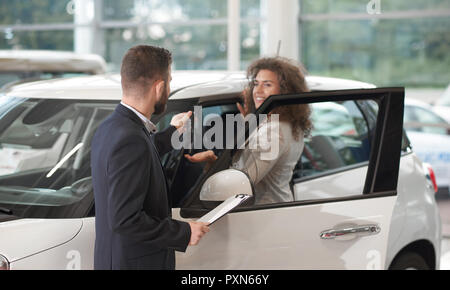 Concessionaria auto in piedi con il client nei pressi di auto e di dare le chiavi. Bella donna felice tenendo la mano e prendere le chiavi da manager. Cliente femmina bianco acquisto di automobili auto in centro. Foto Stock