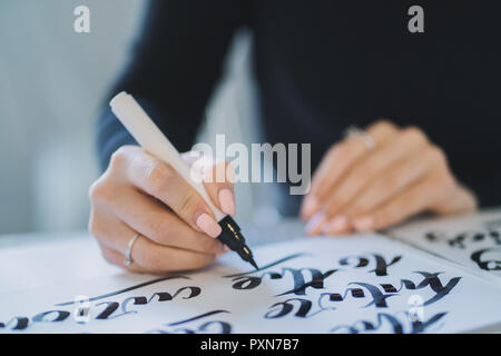 Calligrapher mani scrive una frase sul libro bianco. Inscrivendo ornamentali in lettere decorate. La calligrafia, graphic design, scritte, calligrafia, creatio Foto Stock