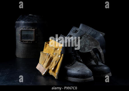 Una vecchia maschera una tuta protettiva per una saldatrice. La salute e la sicurezza sul lavoro abbigliamento per lavoratori di produzione su un tavolo di officina. Sfondo nero. Foto Stock