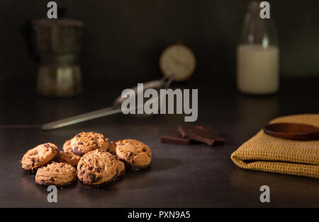 In casa i biscotti al cioccolato su un tavolo da cucina con latte, cioccolato fondente e una tazza di caffè. Foto Stock