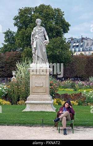 Una giovane donna la lettura di fronte alla statua di La Comedie (1875) da Julien Toussaint Roux nei giardini delle Tuileries a Parigi, Francia. Foto Stock