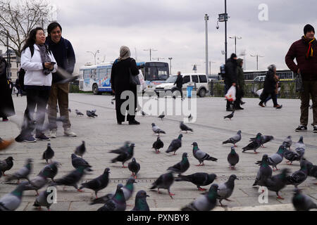 Istanbul, Turchia - 19 Febbraio 2018 : due turisti asiatici stanno prendendo foto dei piccioni in Piazza Eminonu. Anche molte persone turche sono passanti. Foto Stock