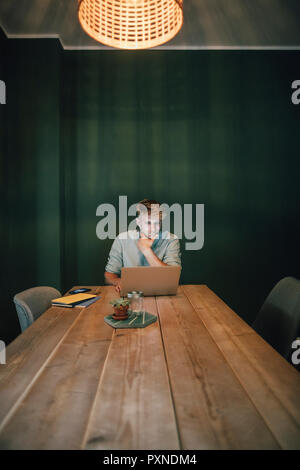Uomo seduto in ufficio, lavora fino a tardi nella sua azienda start-up, utilizzando computer portatile e lo smartphone Foto Stock