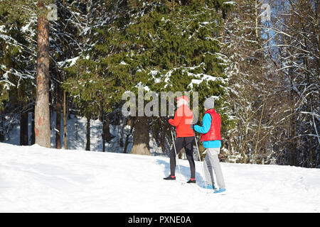 Sportivo contemporaneo coppia senior in activewear andare a sciare in inverno foresta insieme Foto Stock