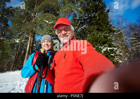Selfie di felice affettuoso coniugi maturi in activewear in piedi nella foresta sul giorno di inverno Foto Stock