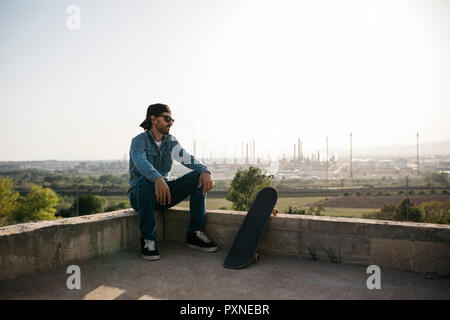 Guidatore di skateboard vestito in abiti casual in appoggio al tramonto Foto Stock