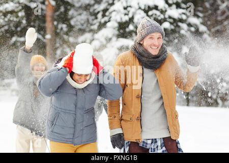Jolly giovani amici a giocare nella neve: eccitato giovane in caldi cappotti a piedi attraverso snowballs nella foresta di inverno Foto Stock