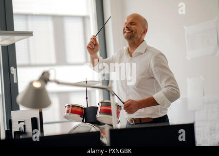 Imprenditore facendo rumore con tamburi nel suo ufficio Foto Stock
