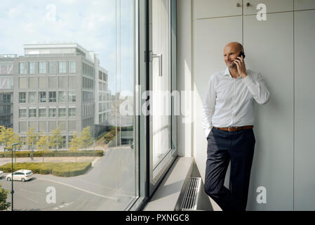 Imprenditore sorridente in piedi nel suo ufficio, parlando sul suo telefono cellulare Foto Stock