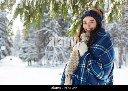 Vita ritratto di sorridente giovane donna in posa nella foresta di inverno in piedi sotto il bellissimo abete e guardando la telecamera, spazio di copia Foto Stock