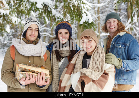 Vita ritratto di due belle coppie giovani in posa nevoso inverno foresta sotto permanente di abete e sorridente in telecamera Foto Stock