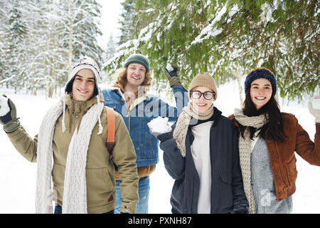 Vita ritratto di quattro giovani felici hanno divertimento in inverno resort azienda snowballs in bella foresta e sorridente in telecamera Foto Stock