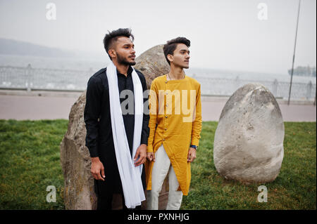Due indiani elegante mans amici in abiti tradizionali poste all'aperto contro grandi pietre. Foto Stock