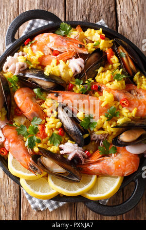 La paella spagnola con gamberetti, cozze, pesce e polipetti close-up in una padella sul tavolo. Verticale in alto vista da sopra Foto Stock