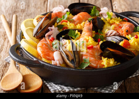 Paella con frutti di mare gamberoni, cozze, pesce e polipetti servita in una padella su una tavola di legno orizzontale. Foto Stock