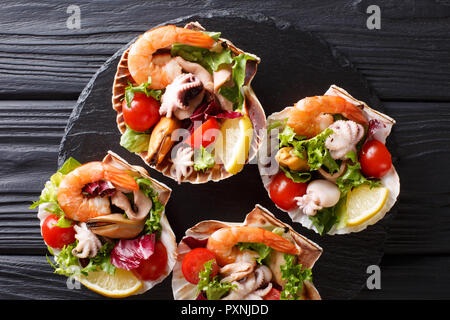 Snack sani insalata di frutti di mare gamberetti, polipetti, le cozze e le conchiglie dei pellegrini e altri pettinidi sono serviti in conchiglie vicino sul tavolo. parte superiore orizzontale vista da abov Foto Stock