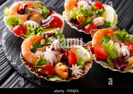 Sana dieta insalata di pesce di gamberetti, polipetti, cozze e calamari capesante con verdure in conchiglie di mare close-up su una tavola nera. horizonta Foto Stock